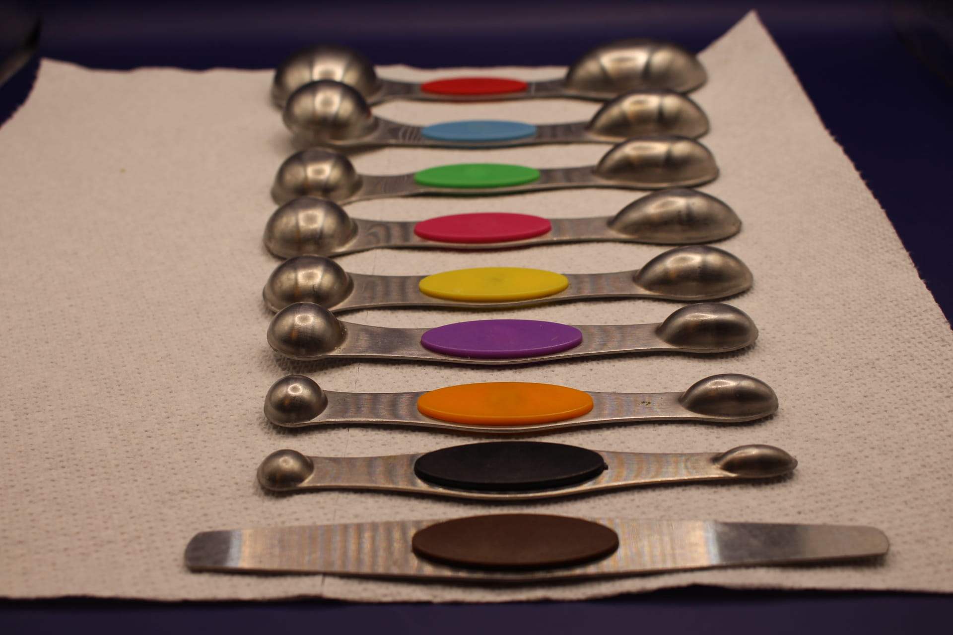 two-ended magnetic measuring spoon set with leveler tool, showing bottoms of spoons, with the smallest spoon at the front