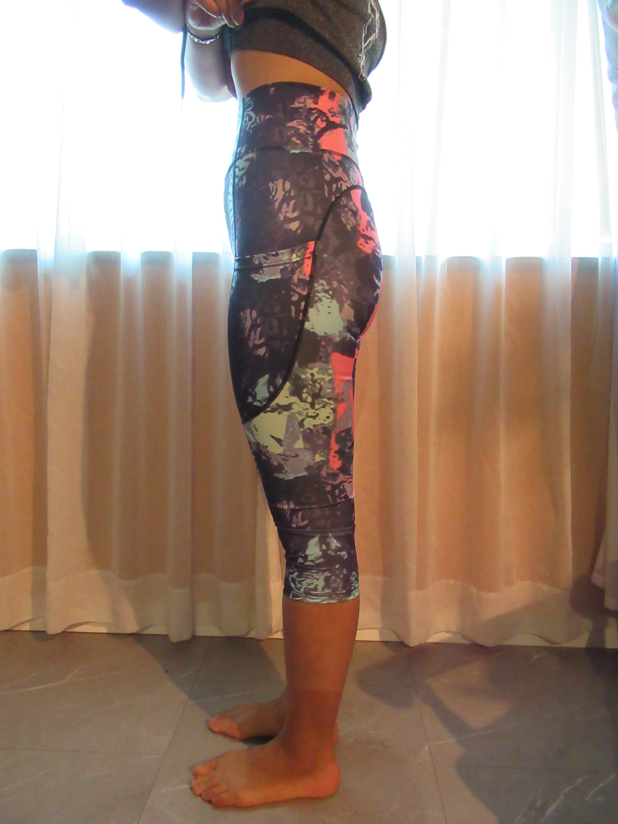 butt-lifting capri pants with big pockets set of three -- purple with pink/green/blue splash design, left side view; trying on, modelling butt-lifter capris on person